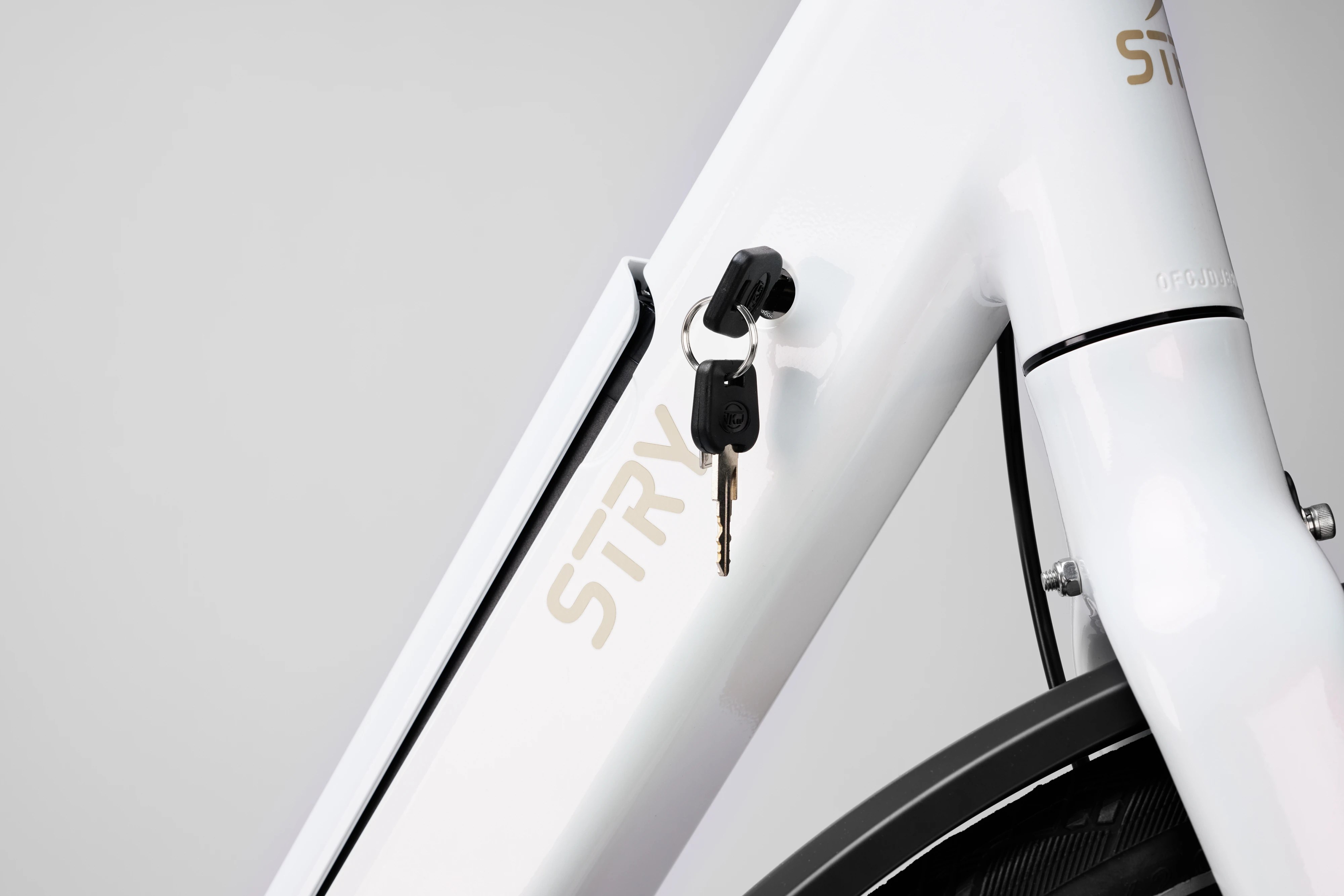 A detailed close-up shot of the battery compartment lock and key mechanism on the sleek white frame of a Stry One electric bicycle.
