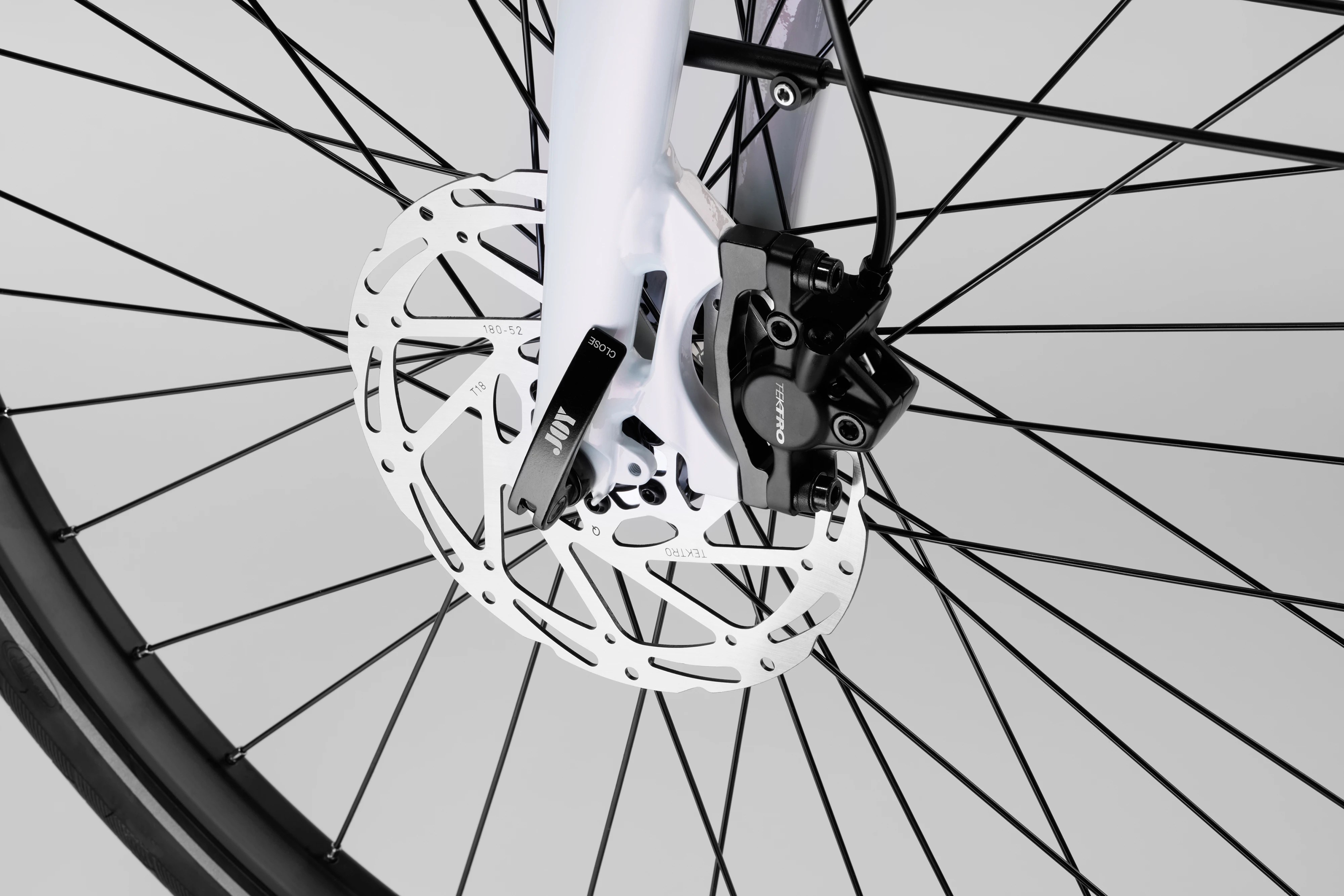 Macro studio shot focusing on the ventilated front disc brake rotor, black brake caliper, and front fork assembly of the pearlescent white Stry One electric bicycle.
